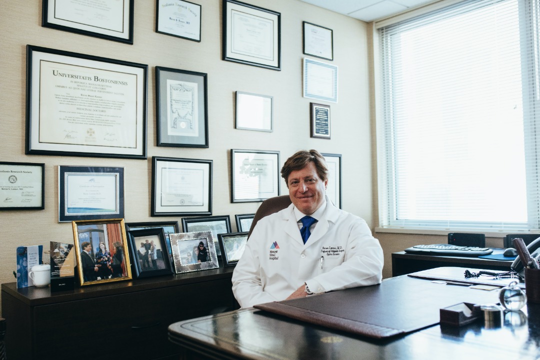  A doctor sitting on his desk and smiling at the camera.