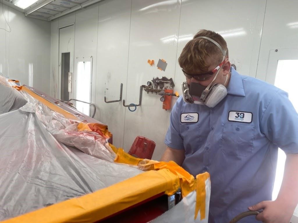 AJ Dorman paints a car in a spray booth in Auto Body repair class using a spray gun.