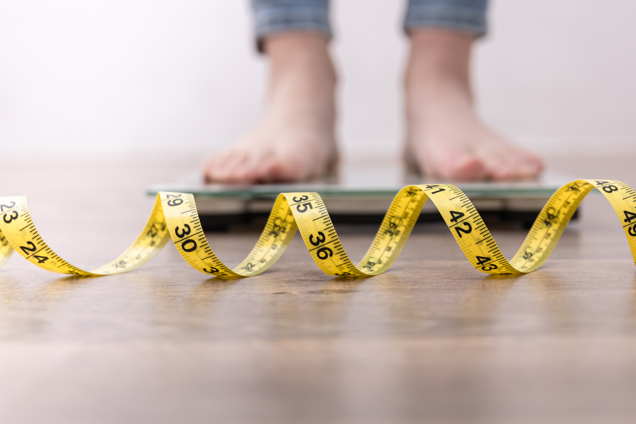 Female stepping on a weighing scale with a measuring tape in front