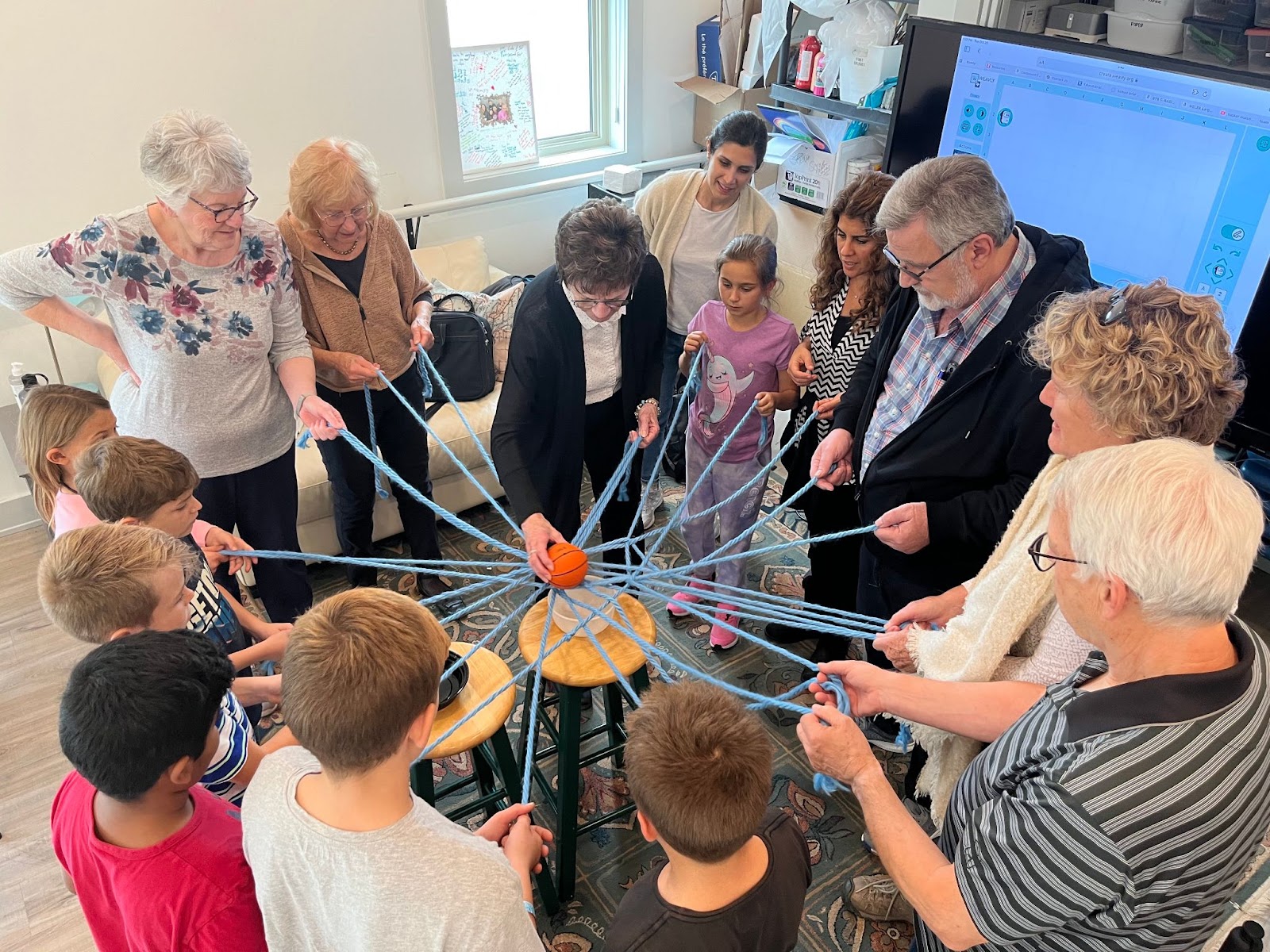 Several people are holding end of multiple strings arranged in a form of spider web. There is a ball in the middle of this ner. 