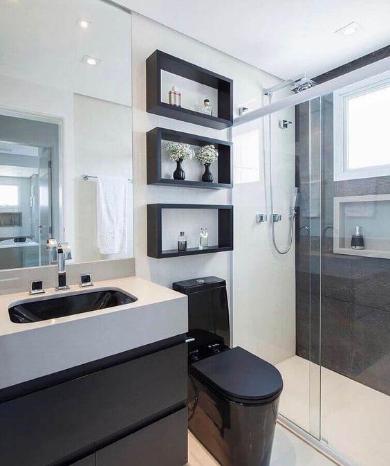 Banheiro com paredes brancas, parede lateral da área do box preta, nichos pretos, bancada da pia branca, com gavetas do armário pretas e vaso sanitário preto.