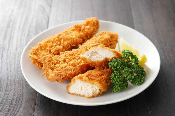 Crispy chicken tenderloins with herbs and a sliced lemon served on a plain white plate