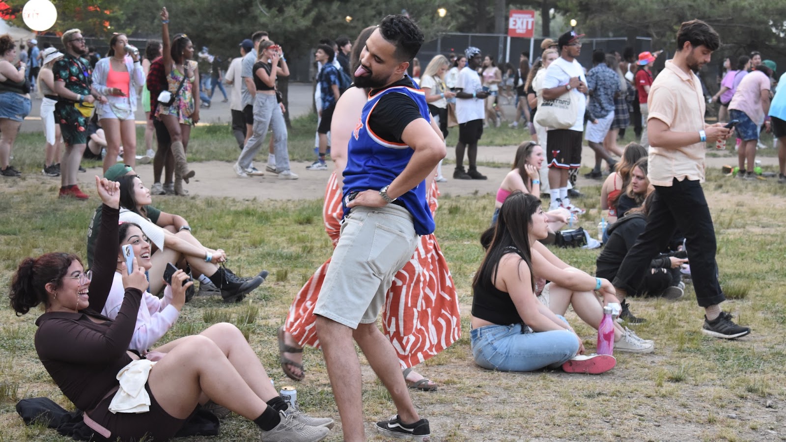 A man dressed in a blue jersey and khaki shorts dancing in front of his friends in the middle of Flushing Meadows Corona Park 