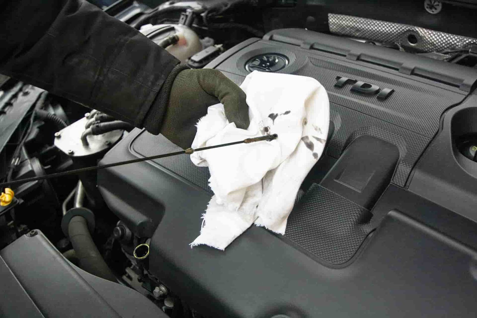 Photo of a mechanic cleaning engine dipstick while checking oil. 