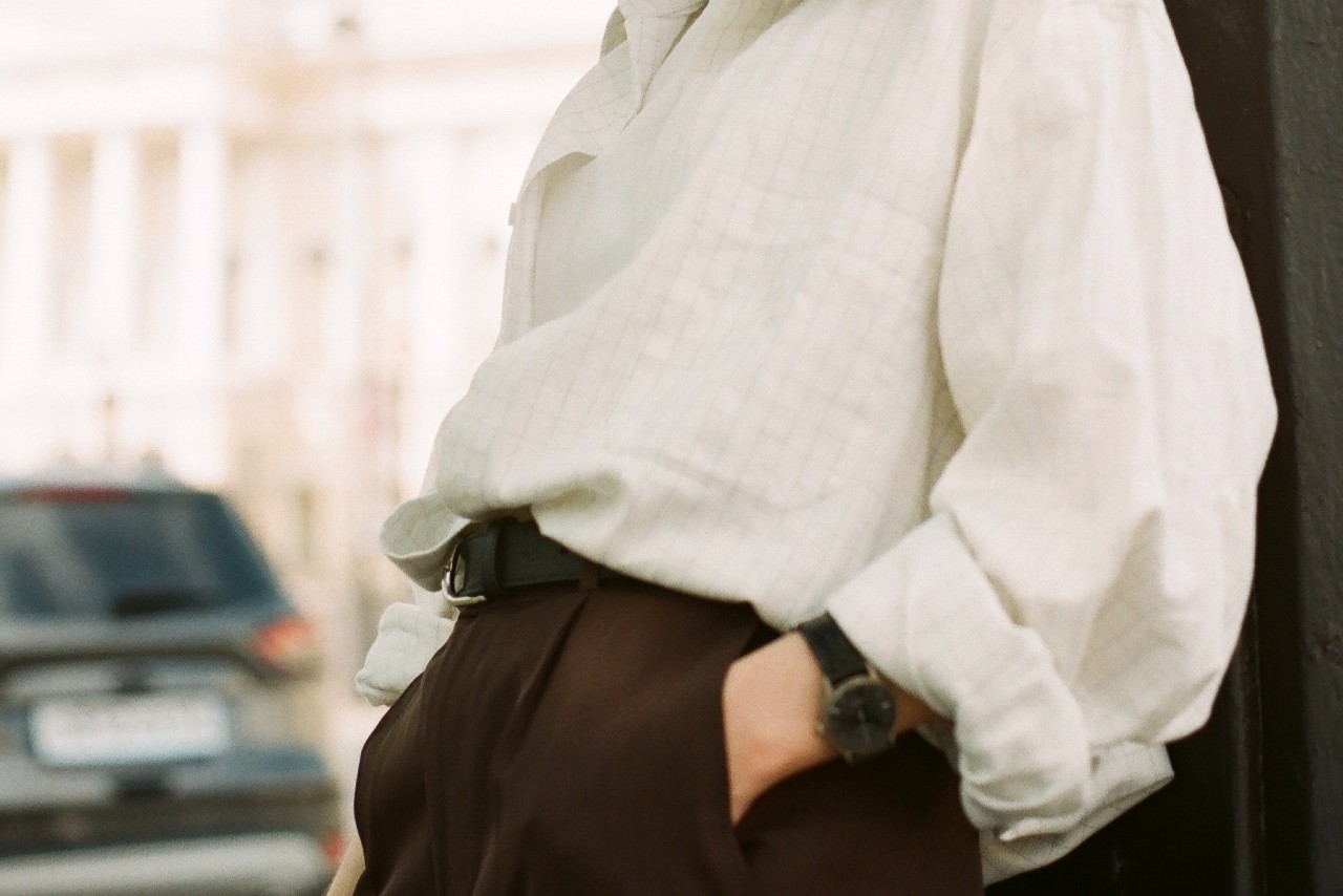 Person leaning against a street post with a finely crafted watch on their wrist. 