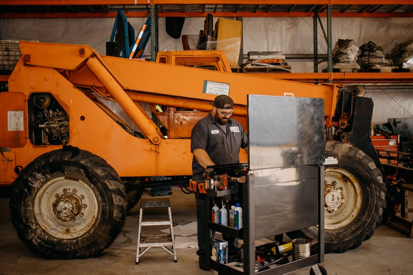 A mechanic looking down at a tray of tools with a giant piece of heavy equipment in the background