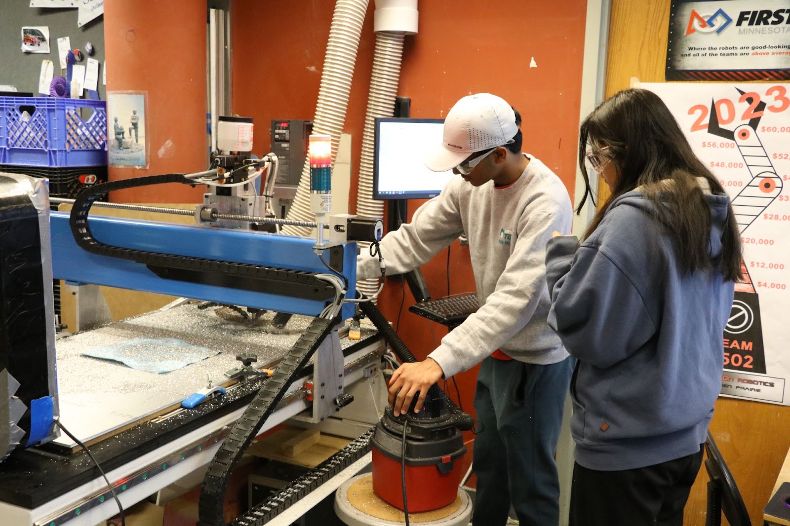 Two students using a metal CNC machine.. They are both looking towards it while it cuts. 