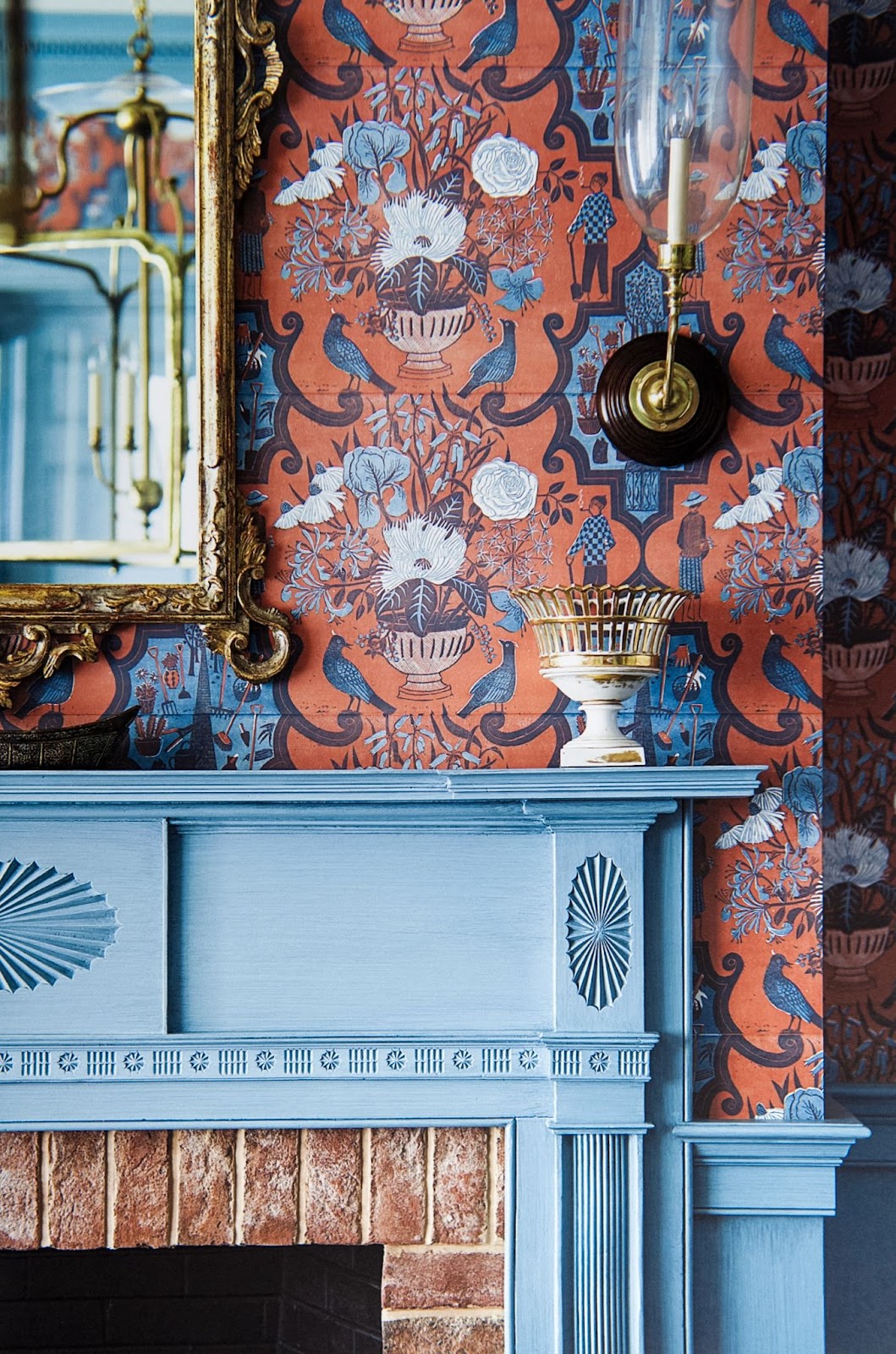 A traditional fireplace mantle finished in medium blue is surrounded by boldly colored wallpaper.