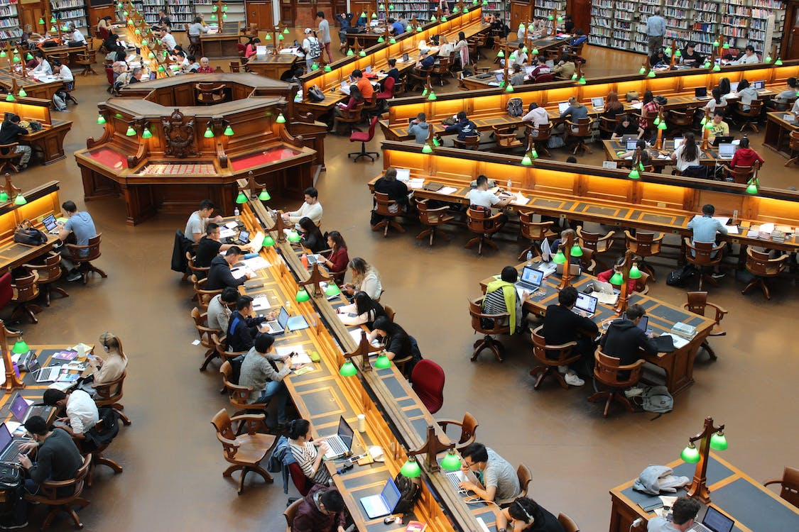 A high-angle photograph of a library filled with rows of books and study tables. 