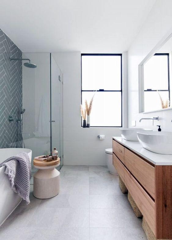 Banheiro com paredes brancas, parede do box com azulejo subway tiles cinza, piso porcelanato cinza claro, bancada e cuba brancas e armário amadeirado