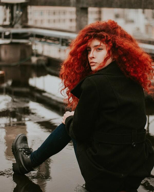 Mulher sentada, olhando para trás, com um cabelo vermelho e cacheado. 