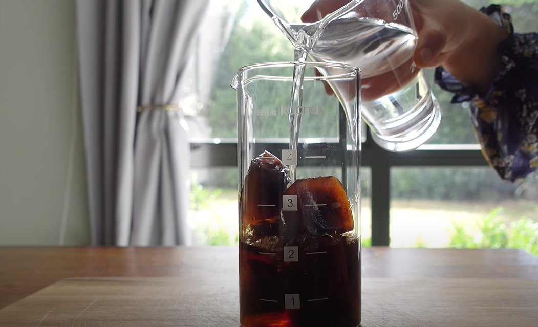 Water being poured into a container with ice and coffee