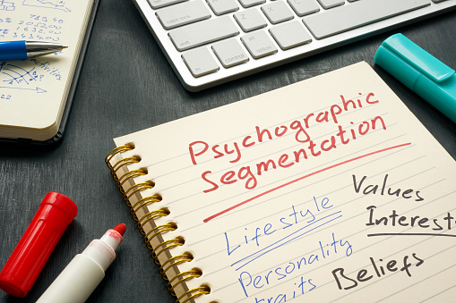 Notepad with the word "Psychographic Segmentation" underlined in red marker. "Lifestyle," "Personality traits," "Values," "Interests," and "Beliefs" are written below the red line.