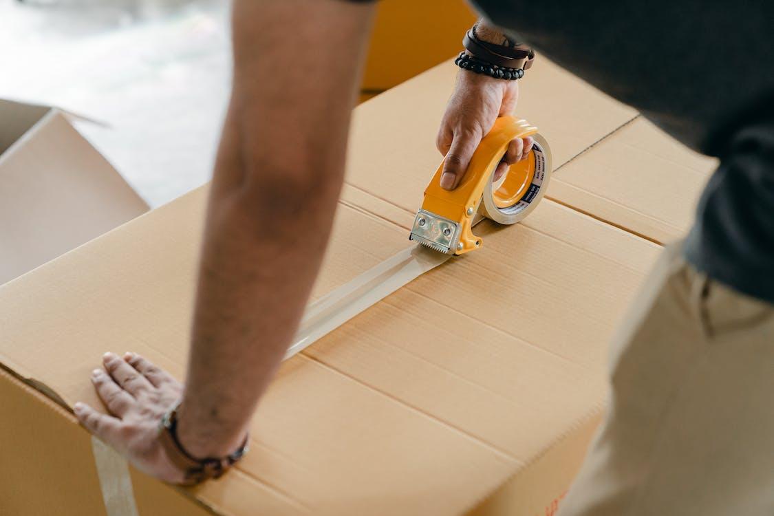 Free Crop faceless man packing box with scotch tape Stock Photo