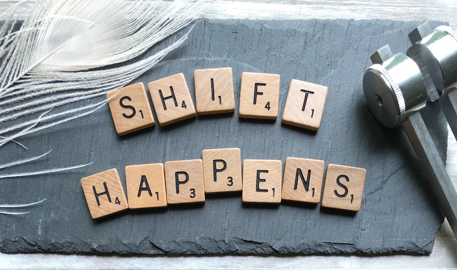 Scrabble tiles arranged on a gray background spelling out the phrase Shift Happens