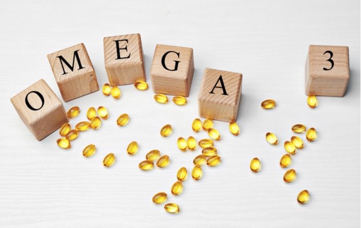 Omega-3 fatty acid supplements laying on a white surface with omega-3 spelled out on wooden blocks around it