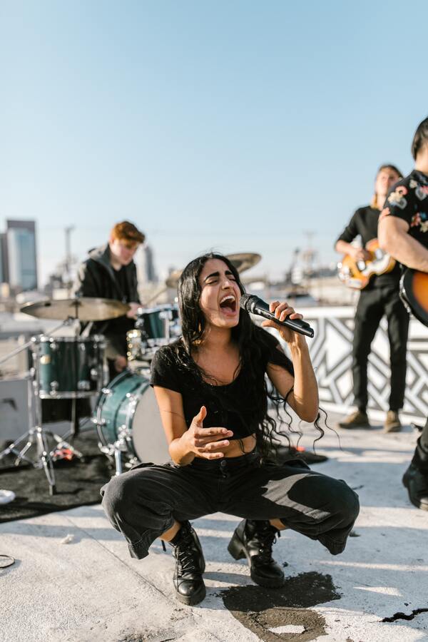 Foto de uma mulher cantando, agachada e, atrás, sua banda. 