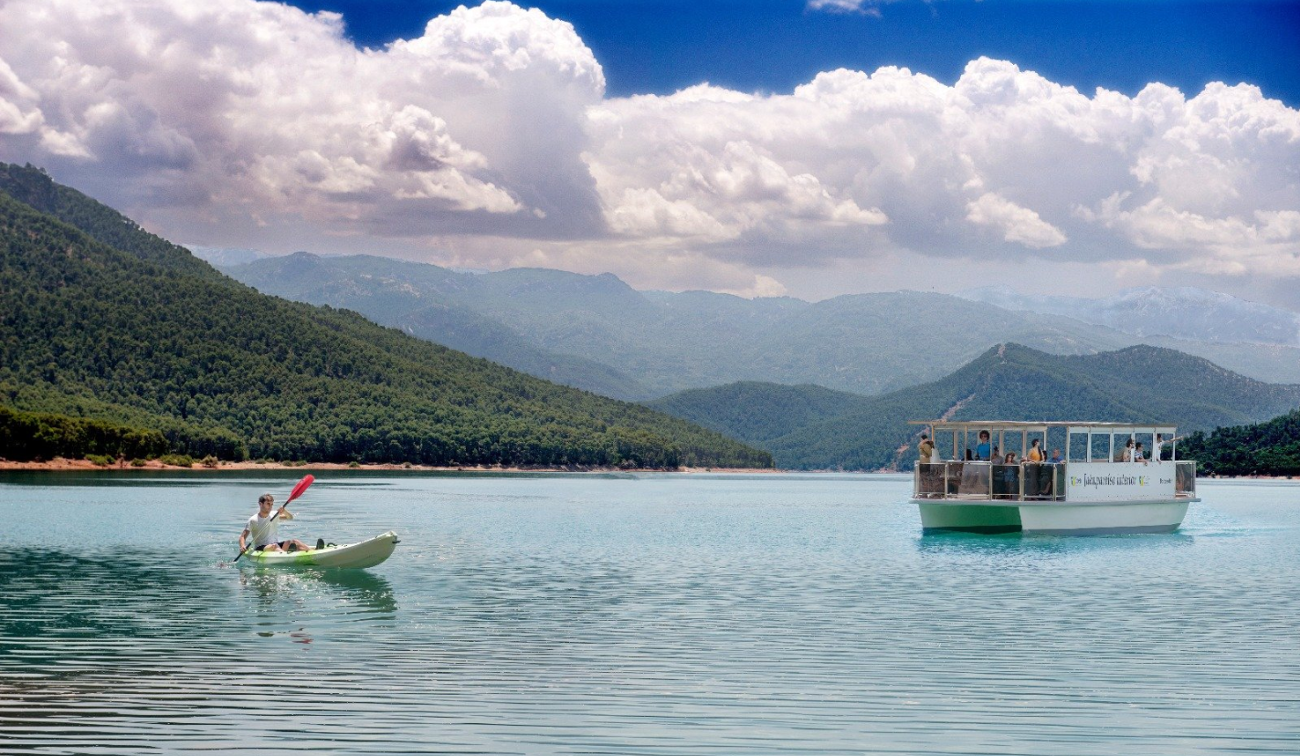 A boat sailing down a river with a mountain range in the background.