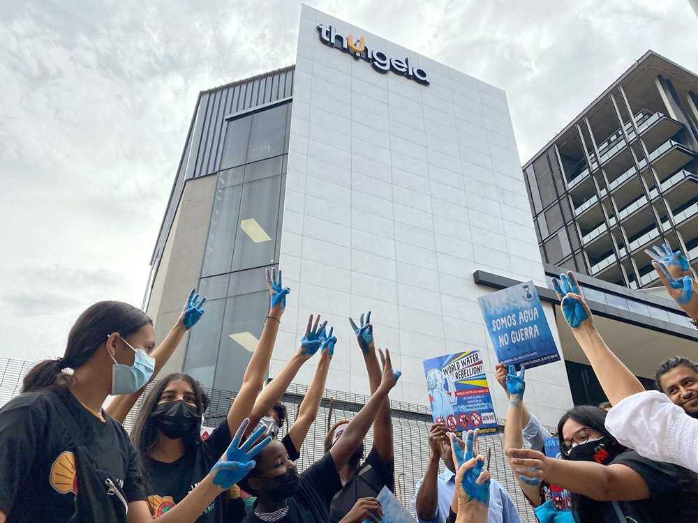 Rebels raise their blue painted hands up in a water salute outside a glass skyscraper branded 'thugela'