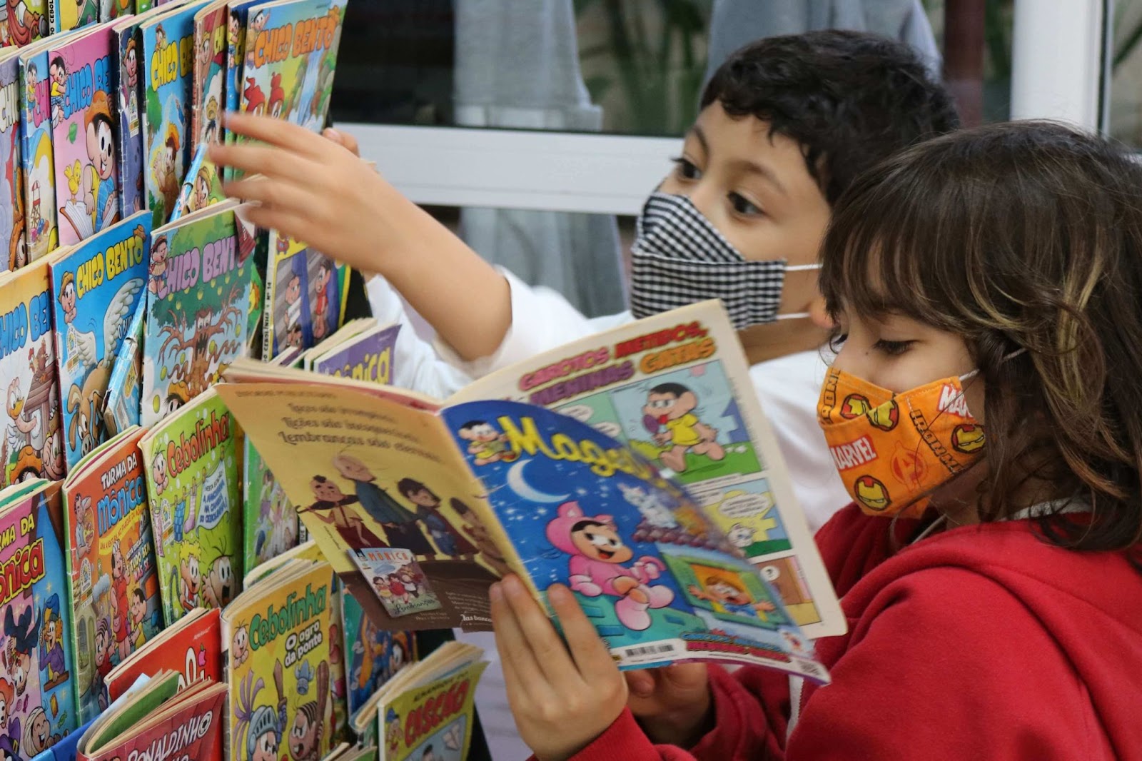 A imagem mostra 2 crianças em frente de uma prateleira de revistas em quadrinhos.