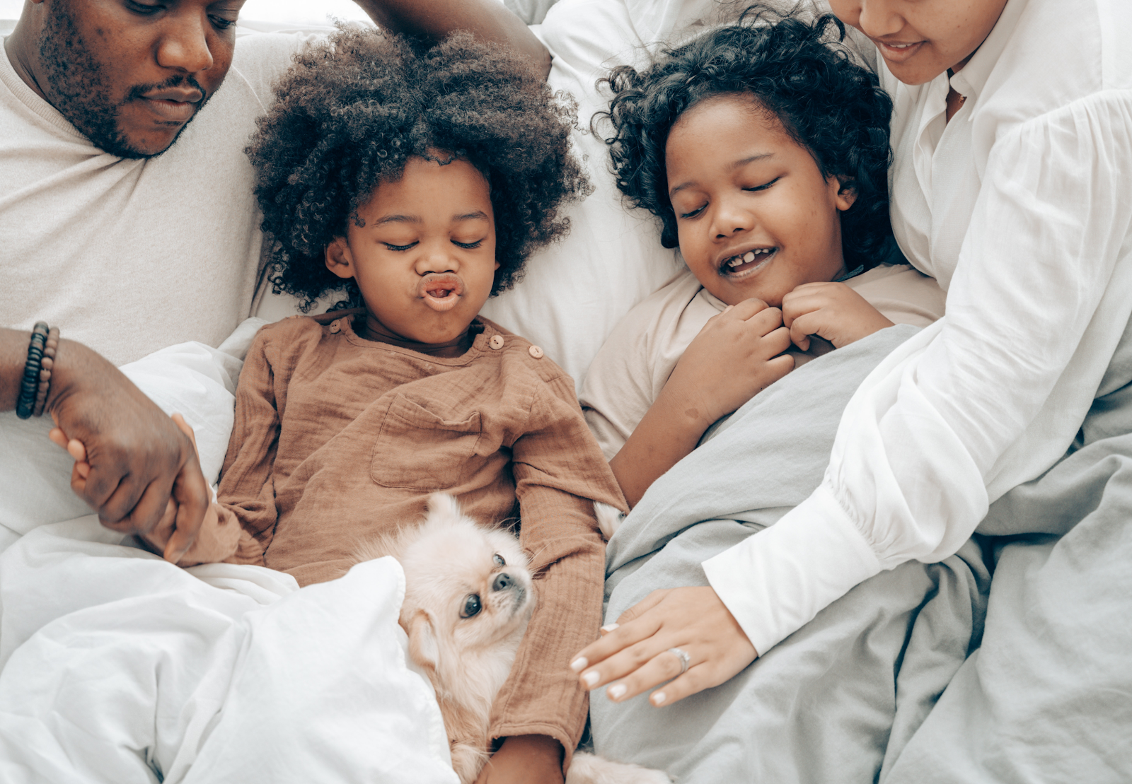 A family of four cuddle in bed with a small dog
