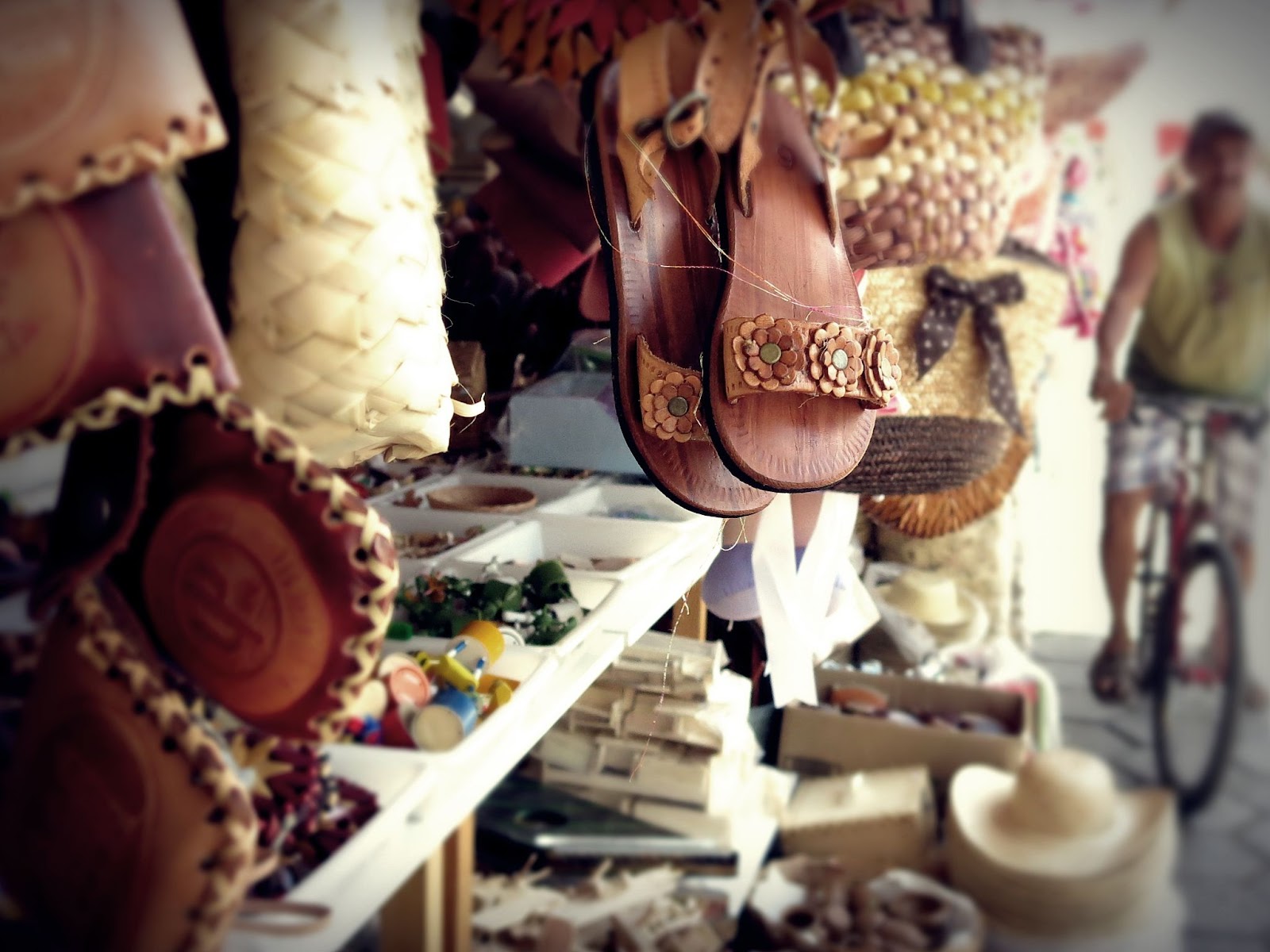 Artigos em exposição na Feira de Caruaru. São vários itens artesanais diferentes, como sandálias de couro, bolsas de palha, chapéus, peões e outros.