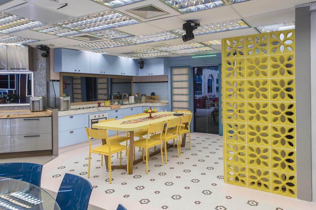 Cozinha com cobogó amarelo, armários azuis, revestimentos retrôs, pastilha na area da pia azul e mesa retangular amarela de 8 lugares.