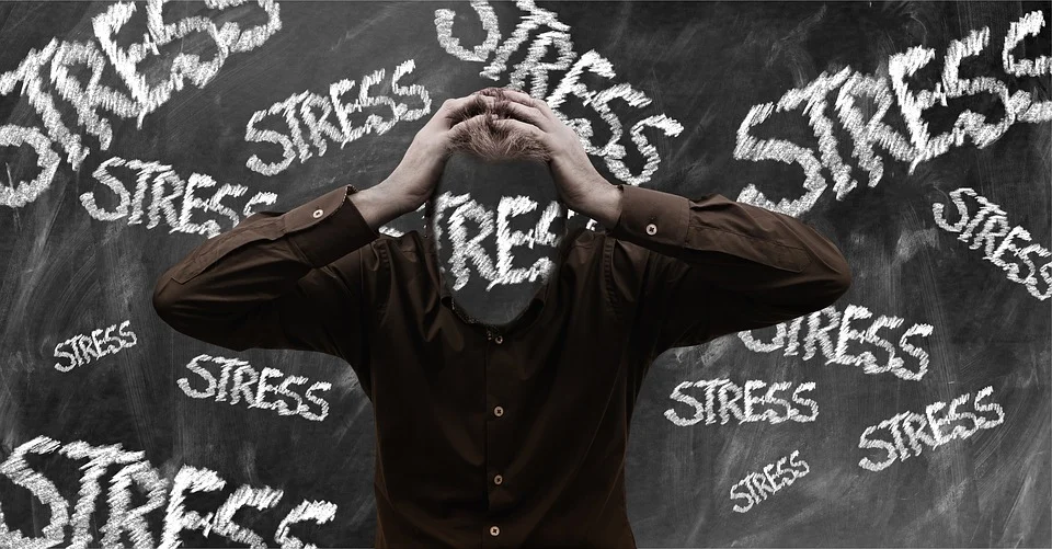 A man holding his head with the word "stress" written multiple times on a chalkboard behind him